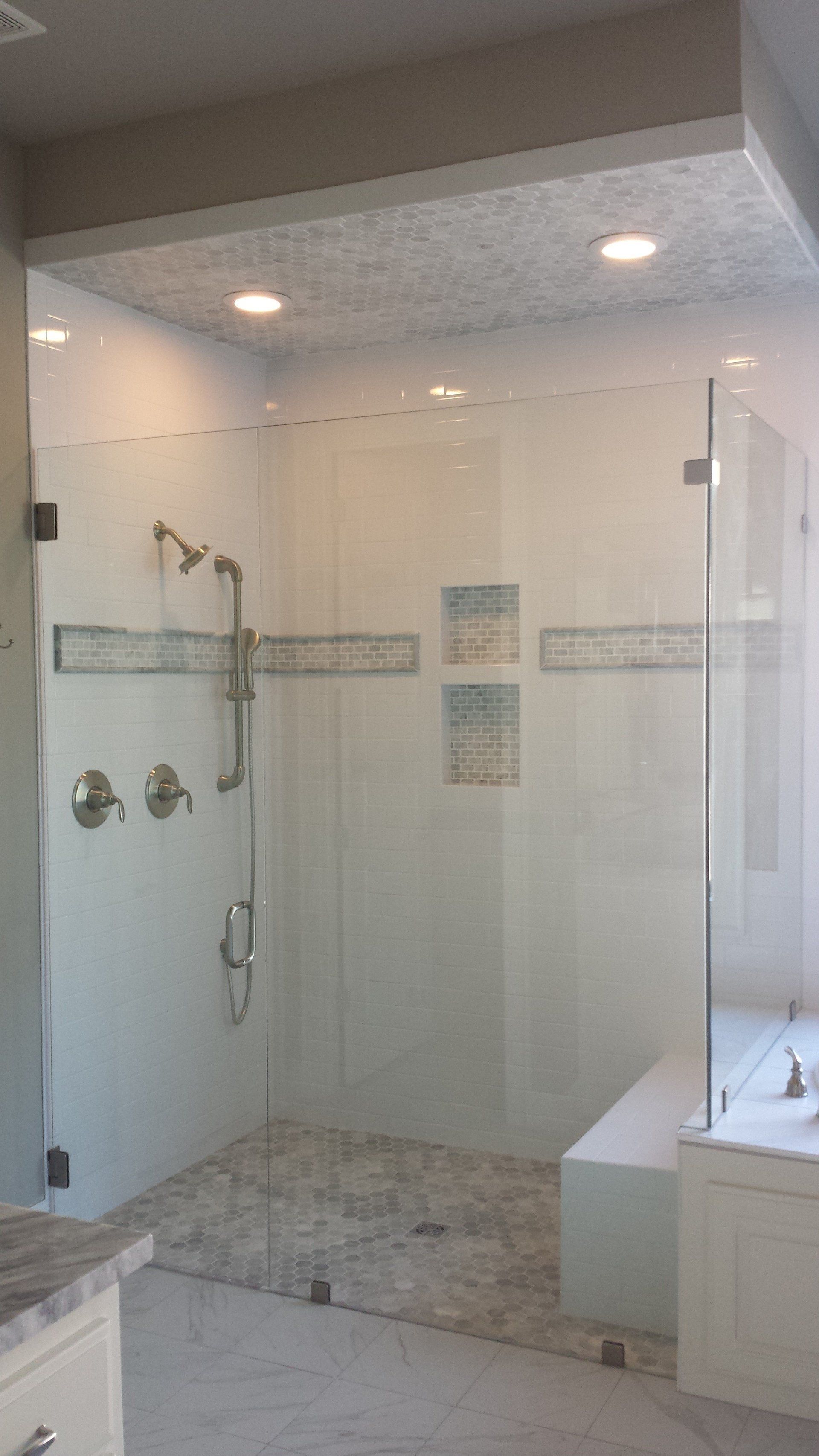 Glass shower with white tile walls, stone floor, and built-in bench.