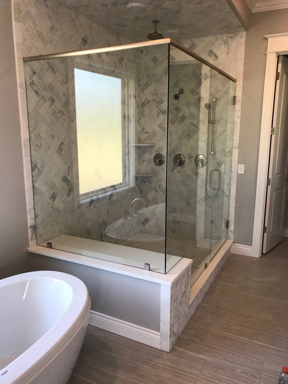 Spacious bathroom with glass shower, soaking tub, and marble-like walls. Sunlight streams through the window.