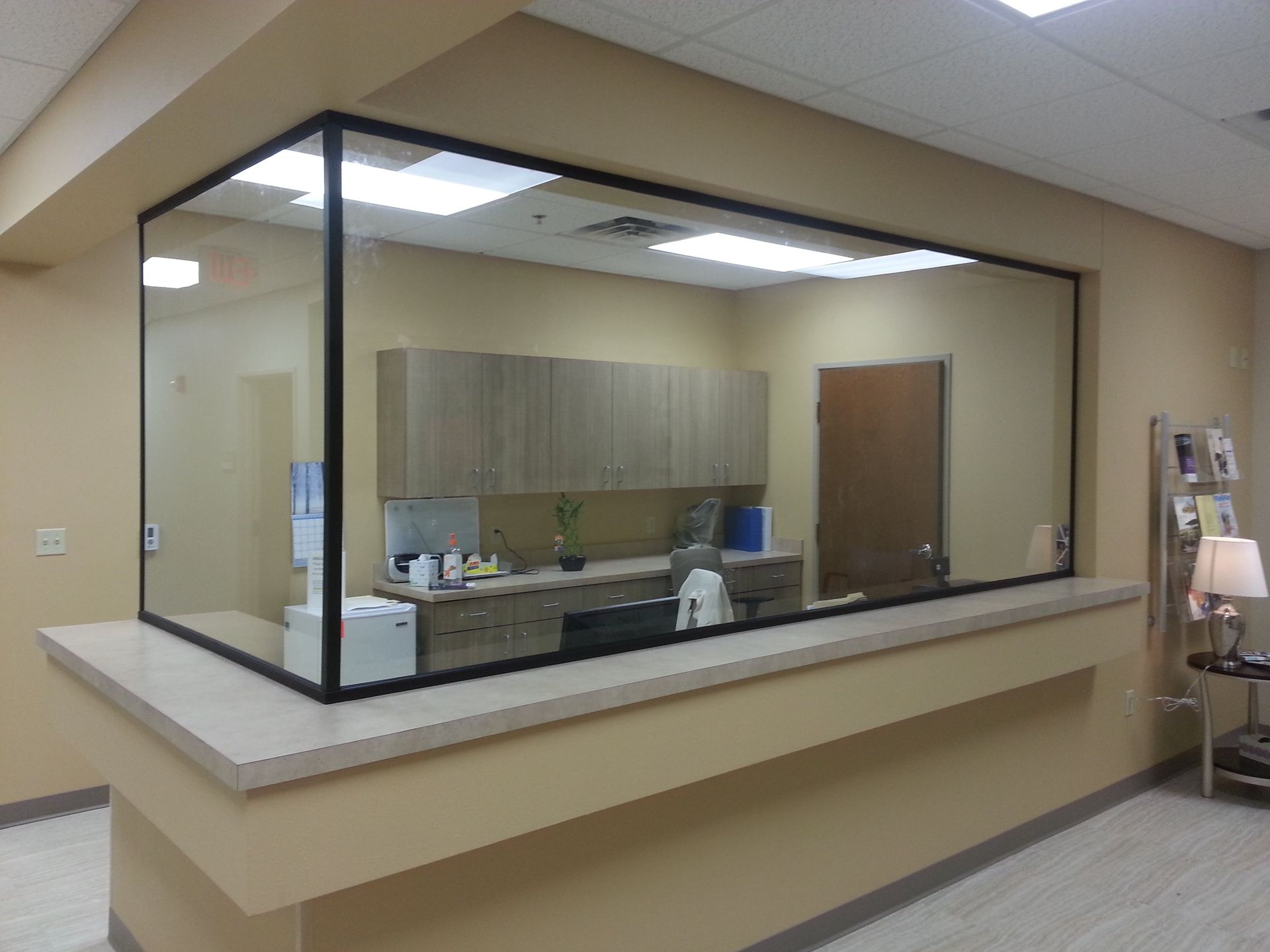 Reception area with glass window, beige walls, and cabinets inside.