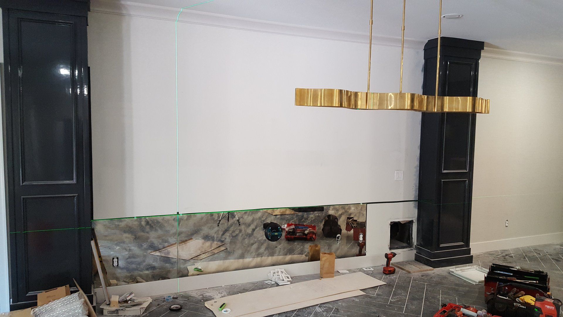 Construction site with bare wall, black pillars, gold chandelier, and electrical components.