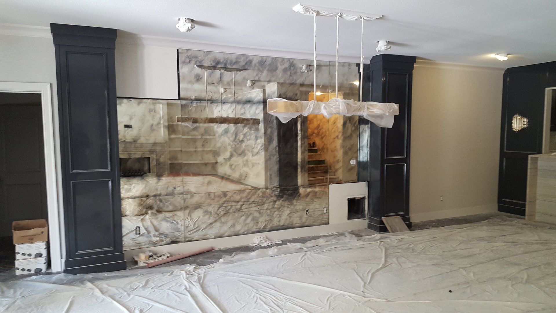 Room under renovation with exposed stone wall, black columns, and white flooring.