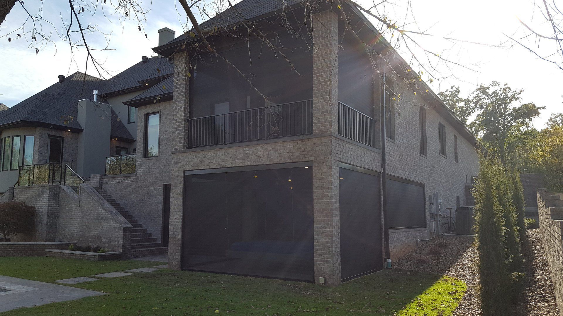 Two-story brick house with dark screens on a covered porch, surrounded by lawn and trees.