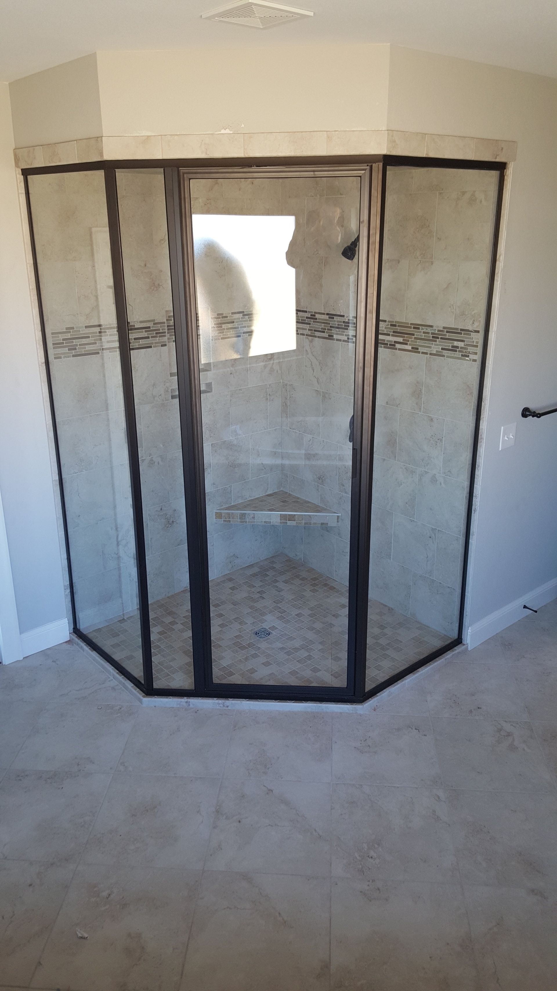 A corner shower with gray tile walls, glass doors with black frames, and a pebble floor.