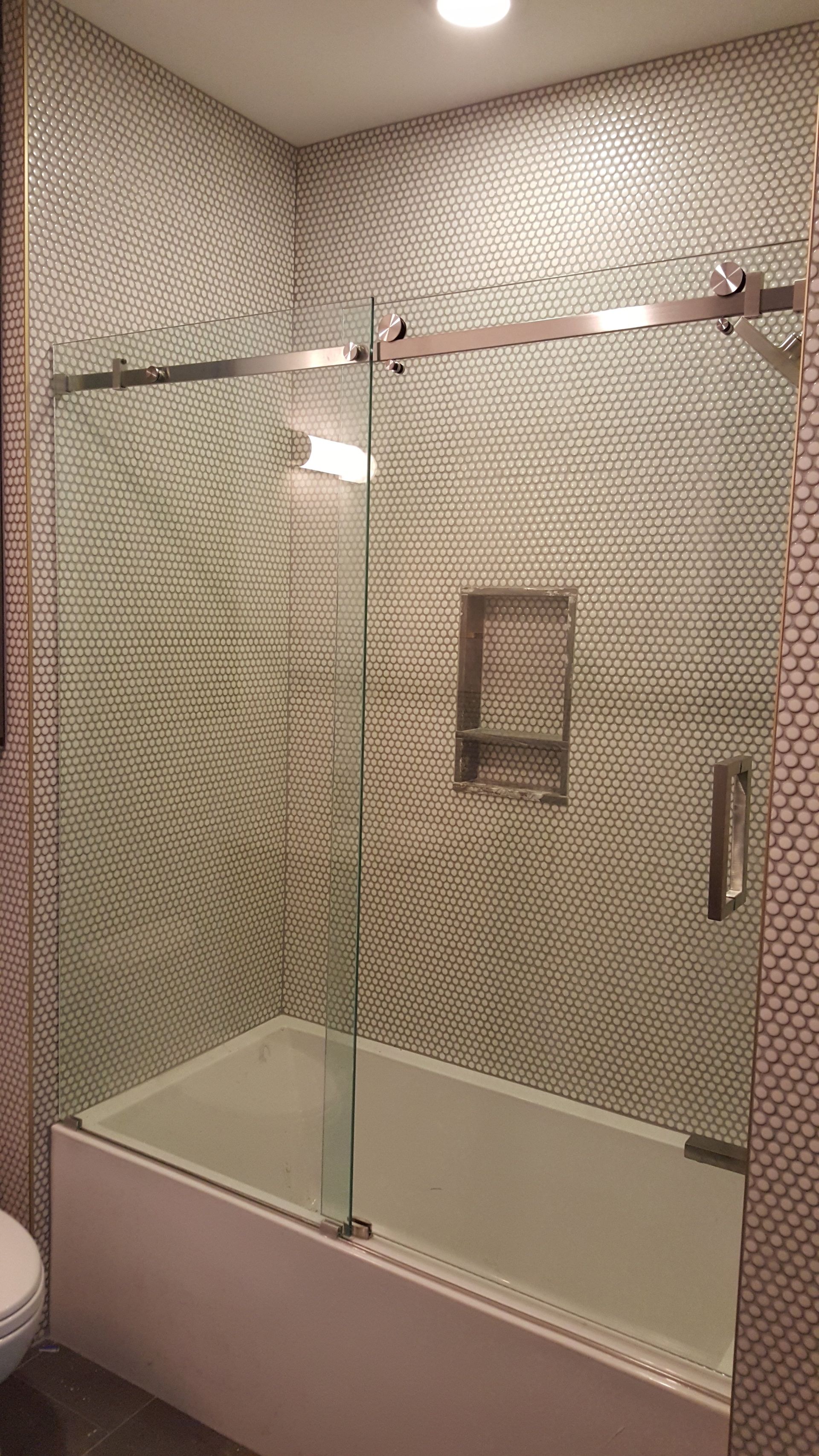 Bathroom with a clear glass shower door over a white bathtub, set against mosaic tile walls.