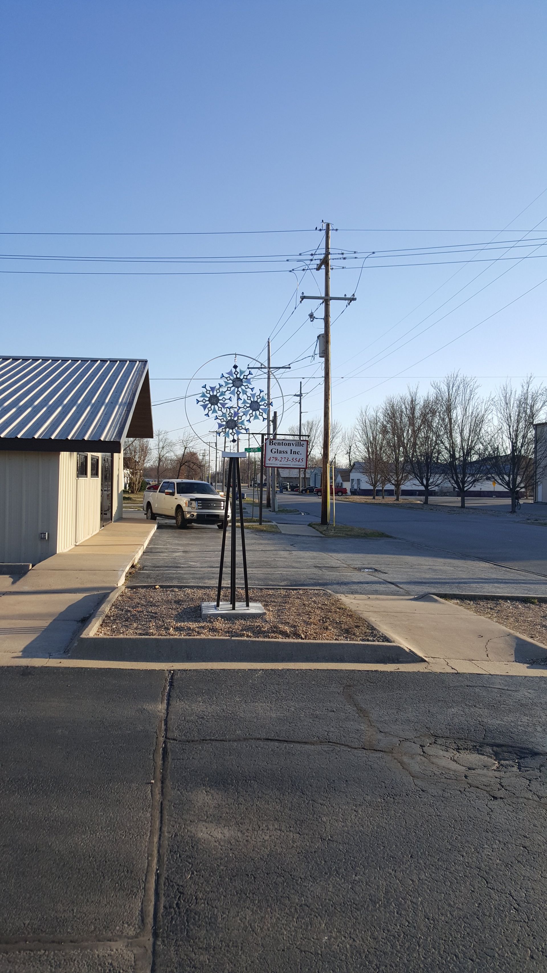 Building, power lines, trees, vehicle, and a flock of birds under a clear blue sky.