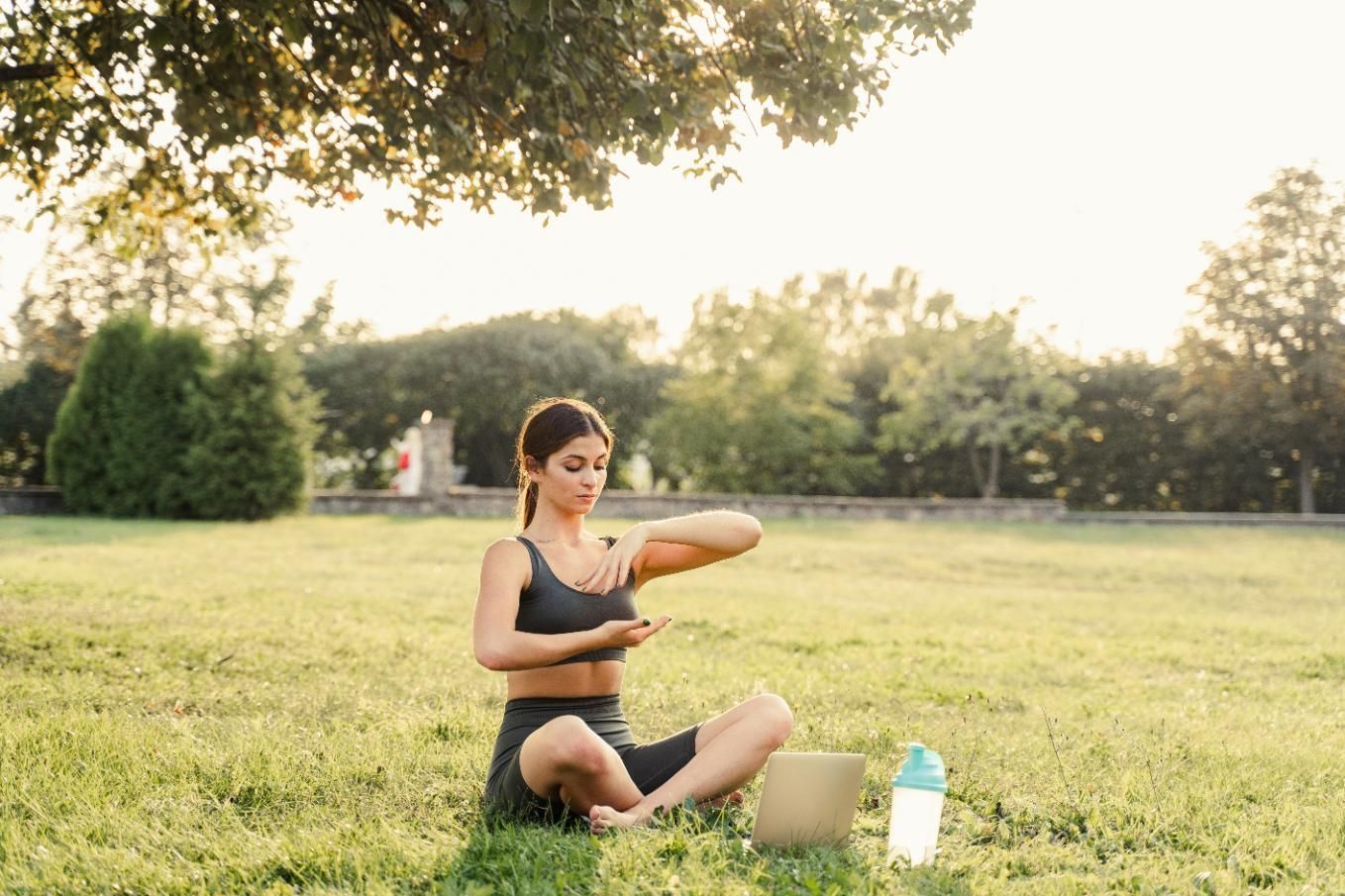 A Woman is Sitting on the Grass in a Park With a Laptop — Alchemy Wellness Centre In Bangalow, NSW
