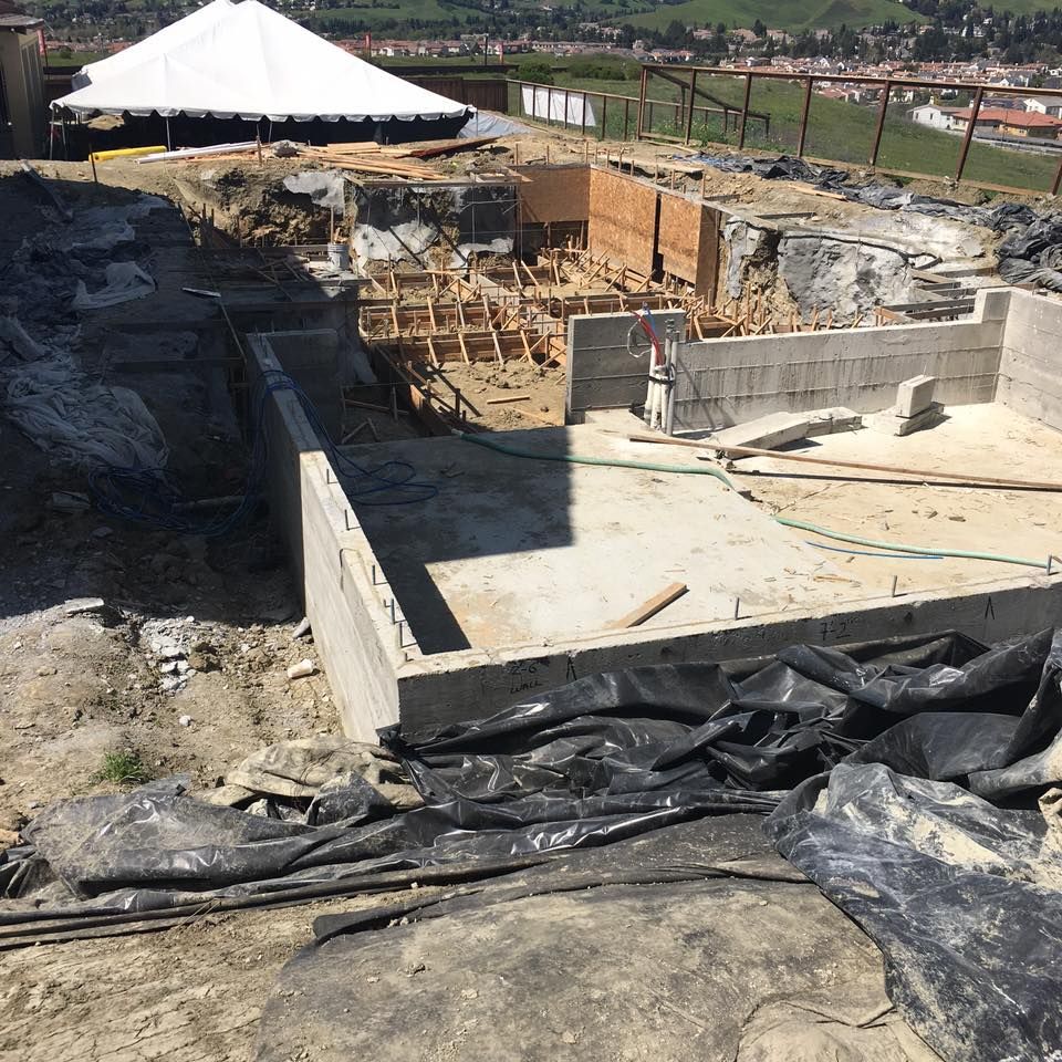 Construction site with exposed concrete foundations, dirt, and temporary tent in the background.