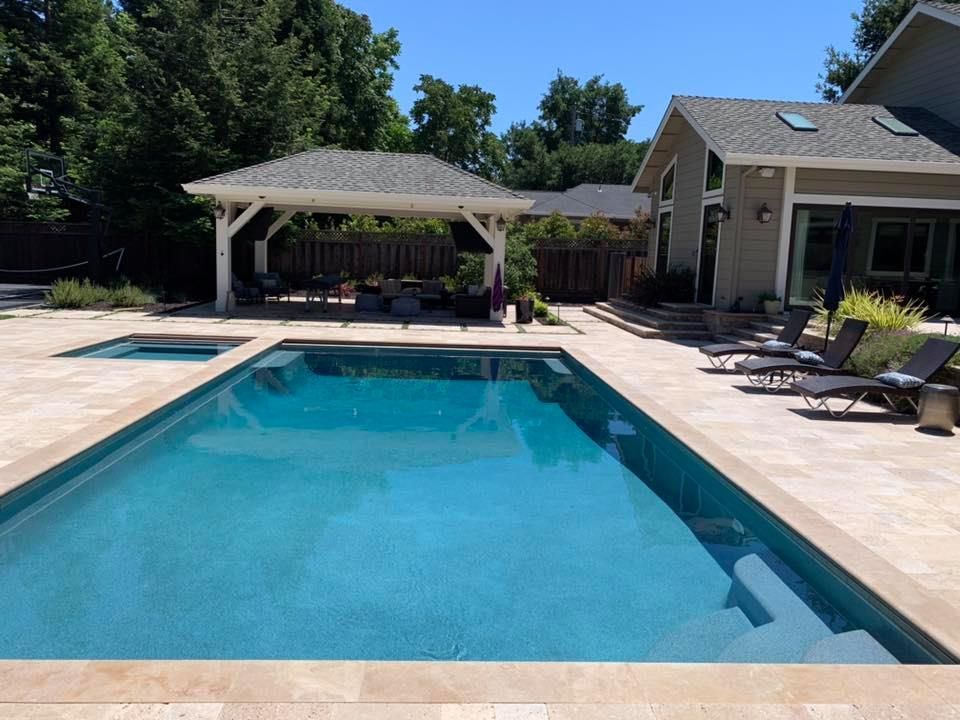 A backyard with a rectangular pool, hot tub, and shaded seating area. House in background.