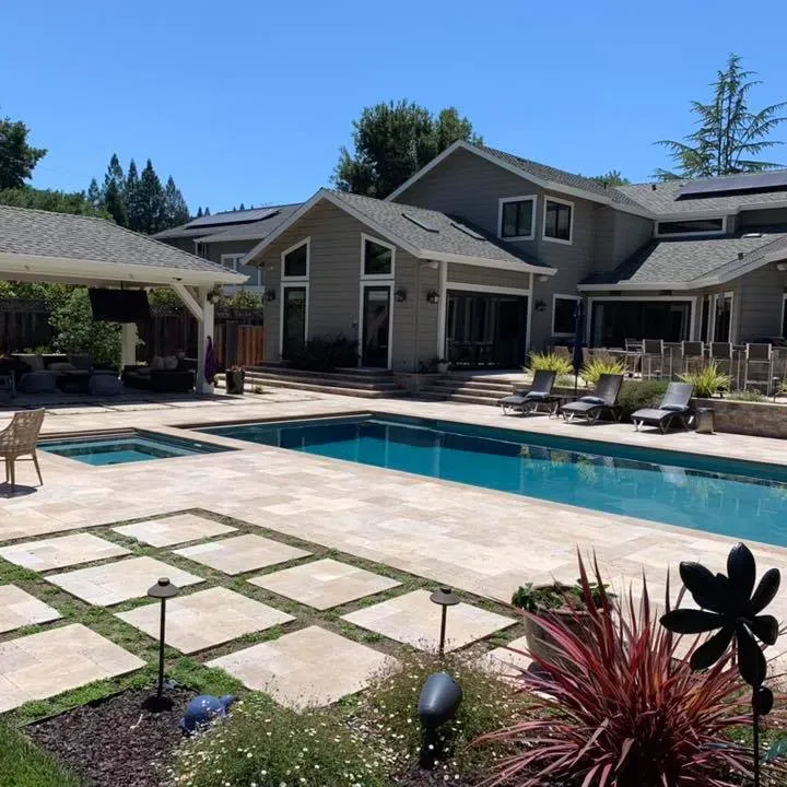 Backyard with a pool, spa, patio, and large house on a sunny day.