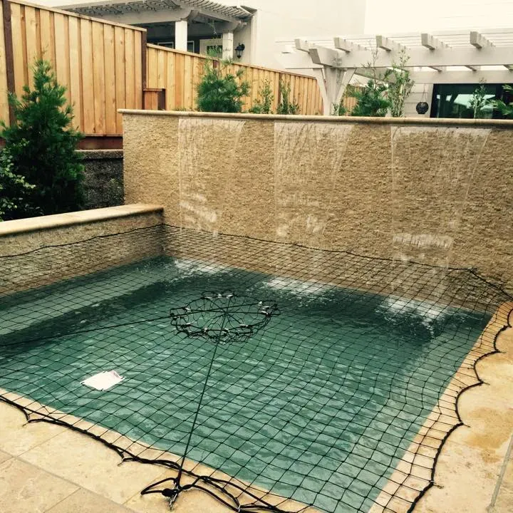 A small, square pool with a waterfall feature, covered by a black safety net.