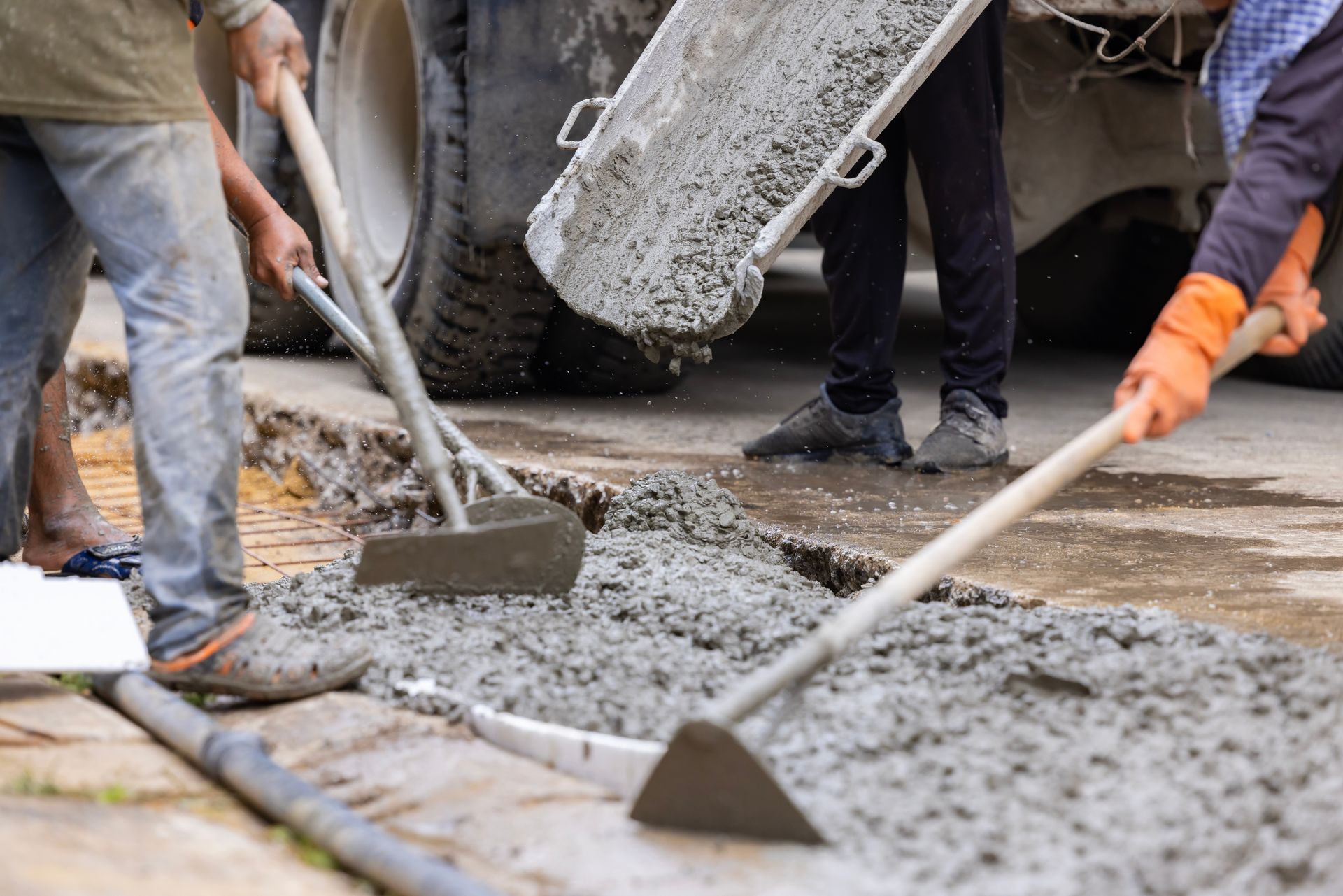 Workers spreading wet concrete on a road with shovels.