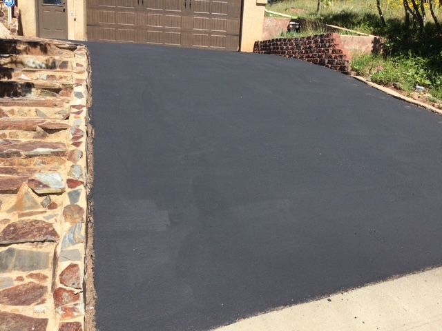 Black asphalt driveway leading to a garage, next to a stone wall.