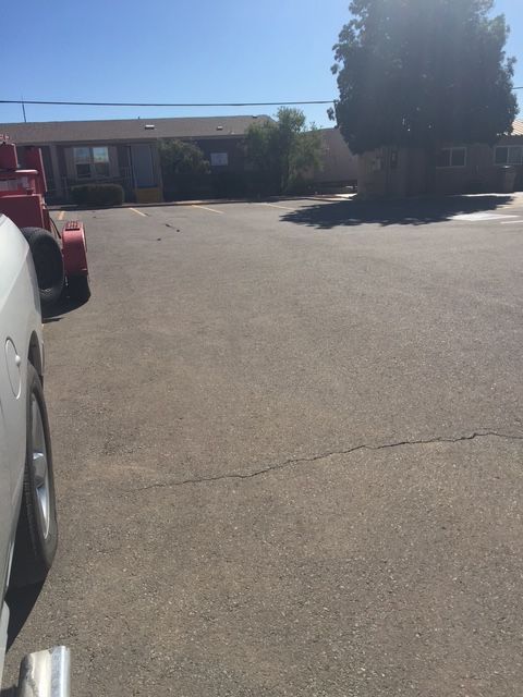 Asphalt lot with a building and a tree, car and trailer on the left, sunny day.