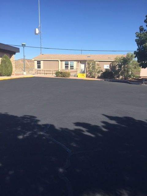 A one-story building with a yellow door sits on a black asphalt surface. Sunny, cloudless sky.