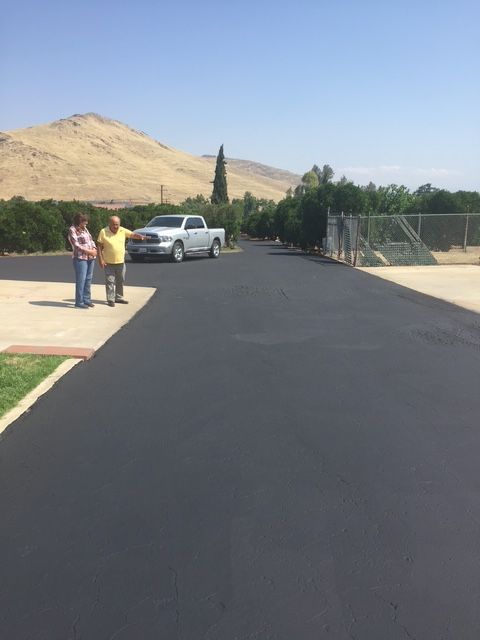 Two people stand on a newly paved driveway, light-colored truck nearby, trees and mountain in the background.