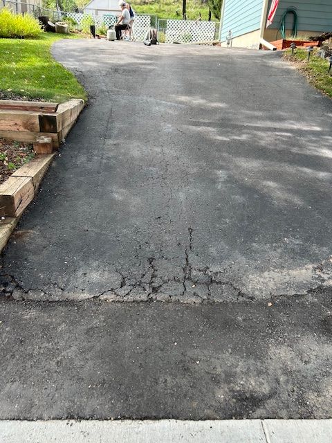 Cracked asphalt driveway leading to a house, with visible damage in the center.