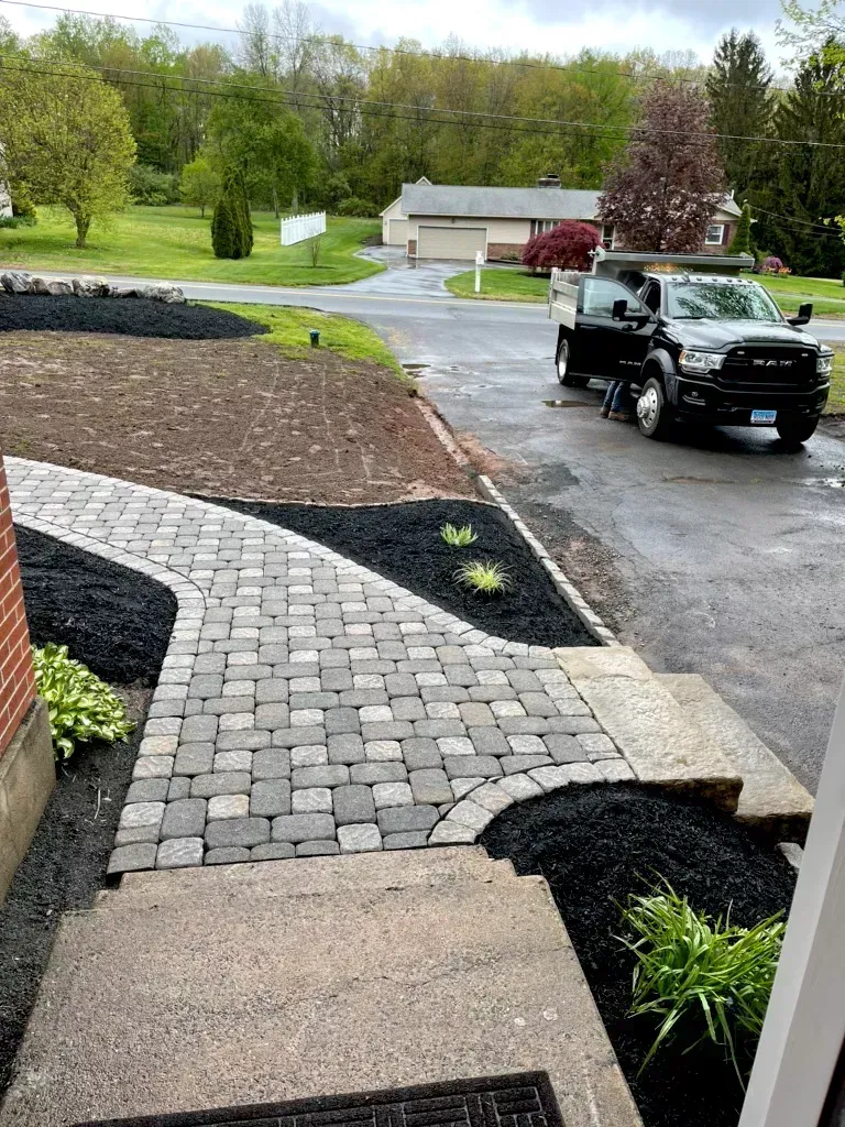 A black truck is parked on the side of the road next to a brick walkway.