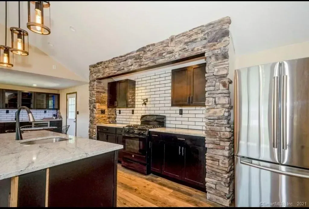 A kitchen with stainless steel appliances and a stone wall.