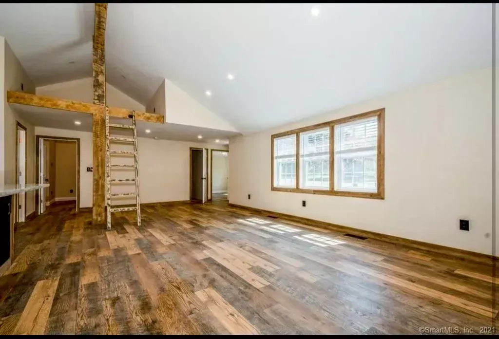 An empty living room with hardwood floors and a ladder.