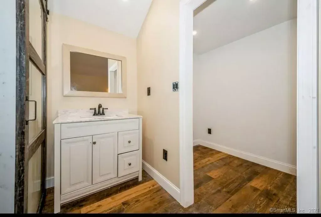 A bathroom with a sink , mirror and hardwood floors.