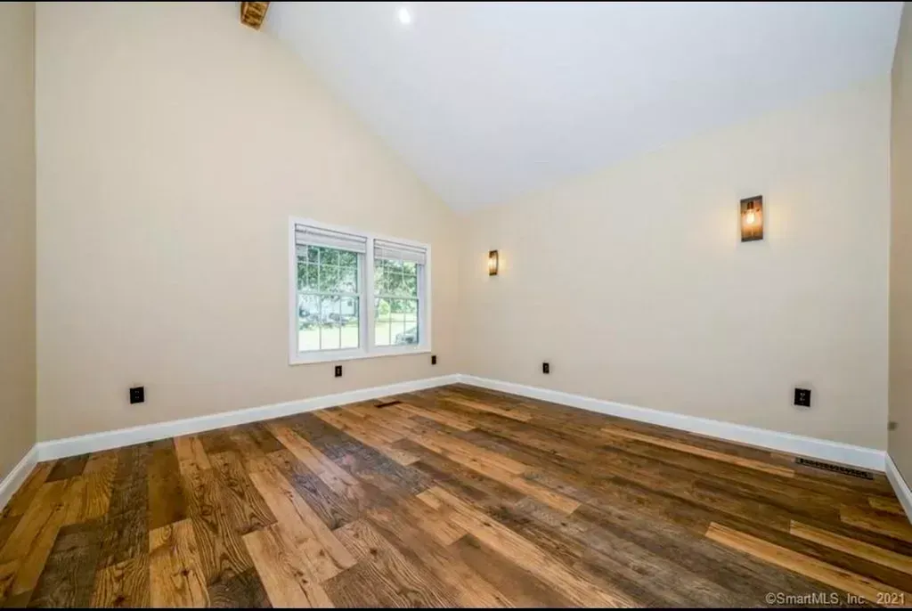 An empty room with hardwood floors and two windows.