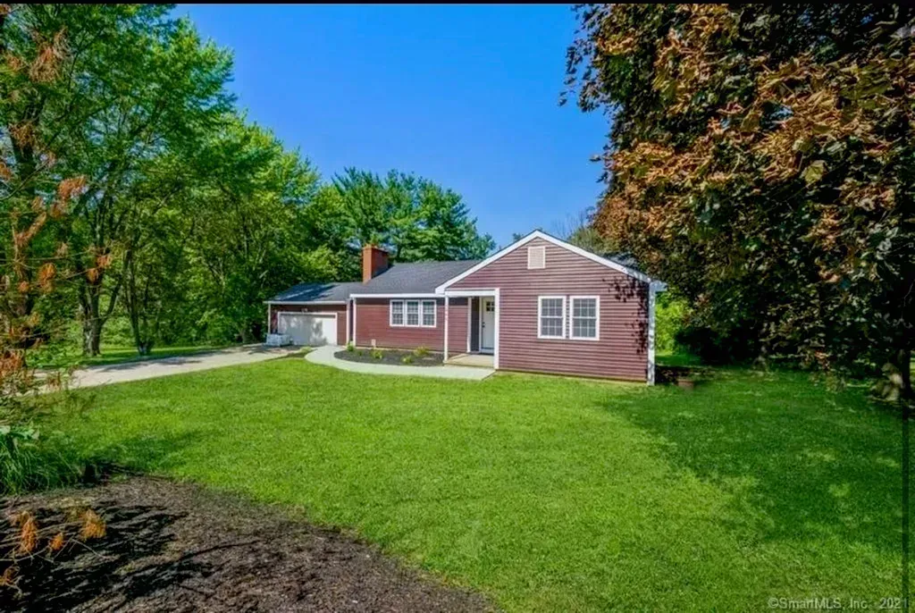 A red house is sitting in the middle of a lush green field surrounded by trees.
