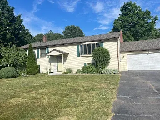 A white house with green shutters and a driveway in front of it.