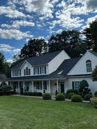 A large white house with a black roof is sitting on top of a lush green lawn.