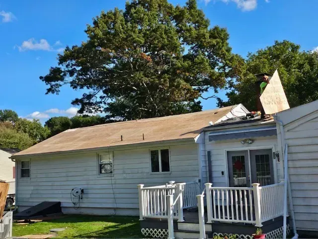 A man is standing on the roof of a house holding a piece of wood.