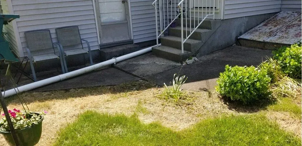 A concrete walkway leading to a house with stairs and chairs.