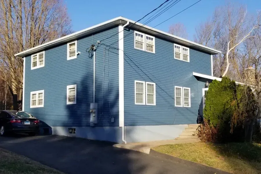 A blue house with white trim and a car parked in front of it.
