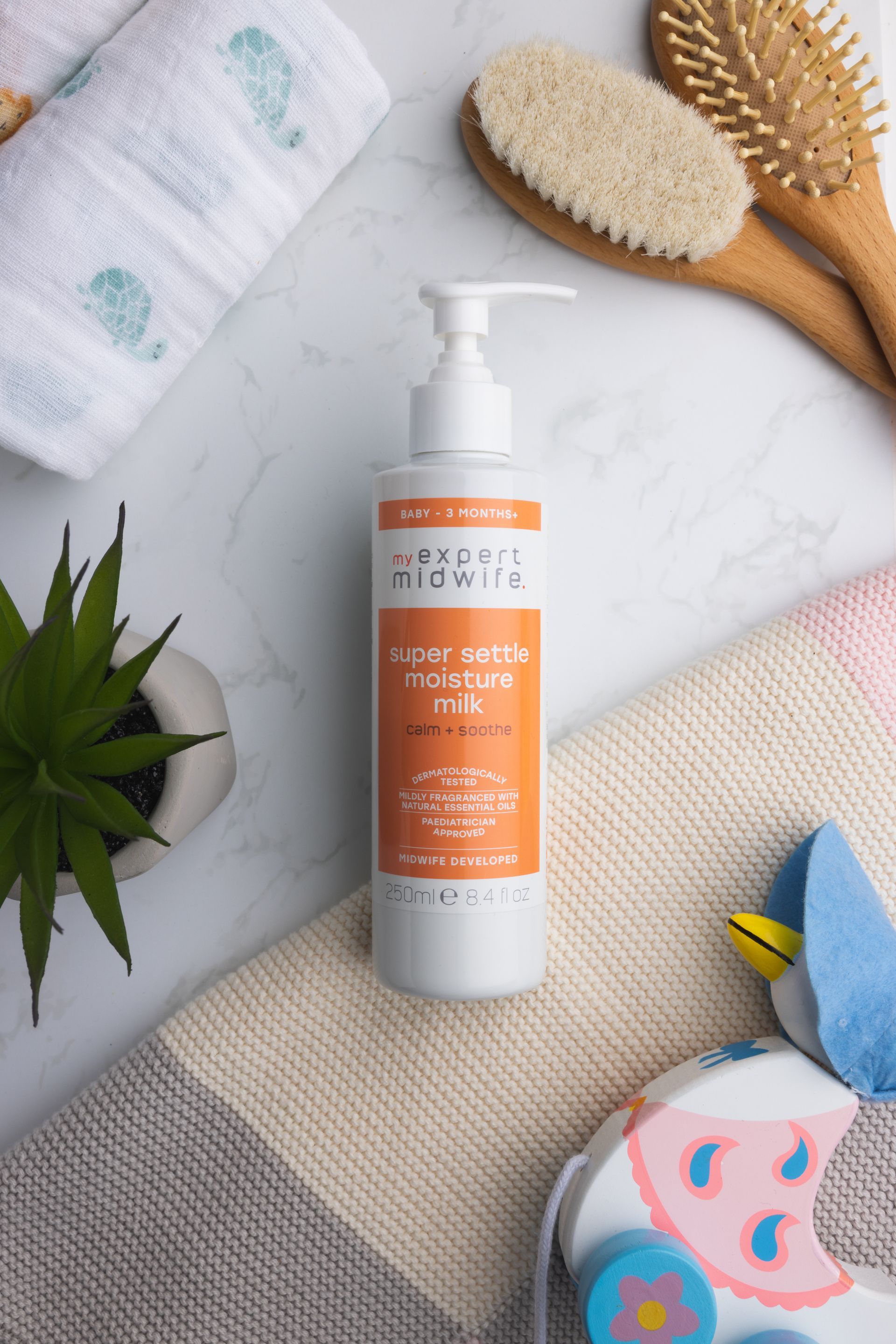a bottle of baby lotion is sitting on a towel next to a plant and brushes .