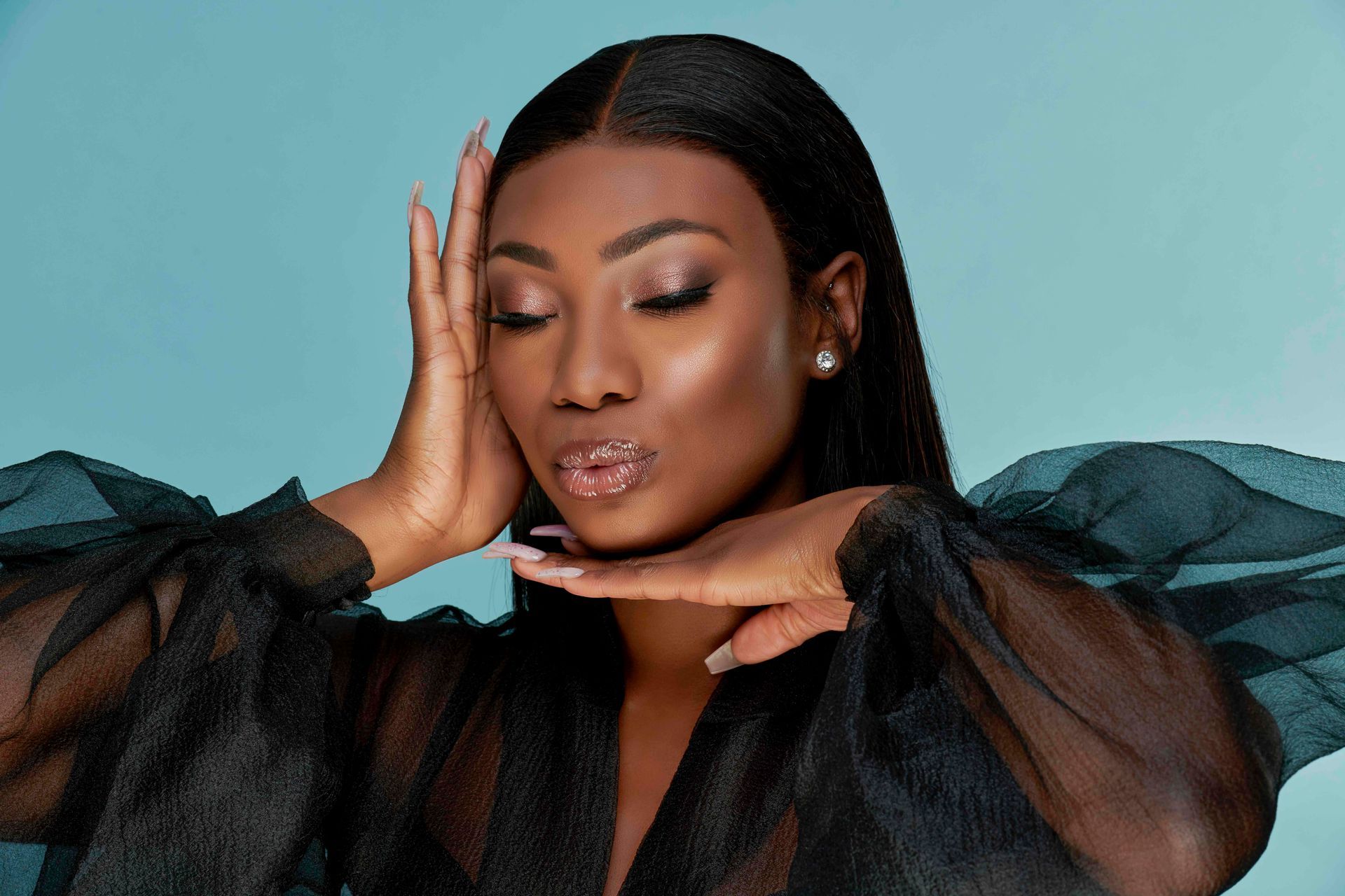 A woman in a black dress is covering her face with her hands.