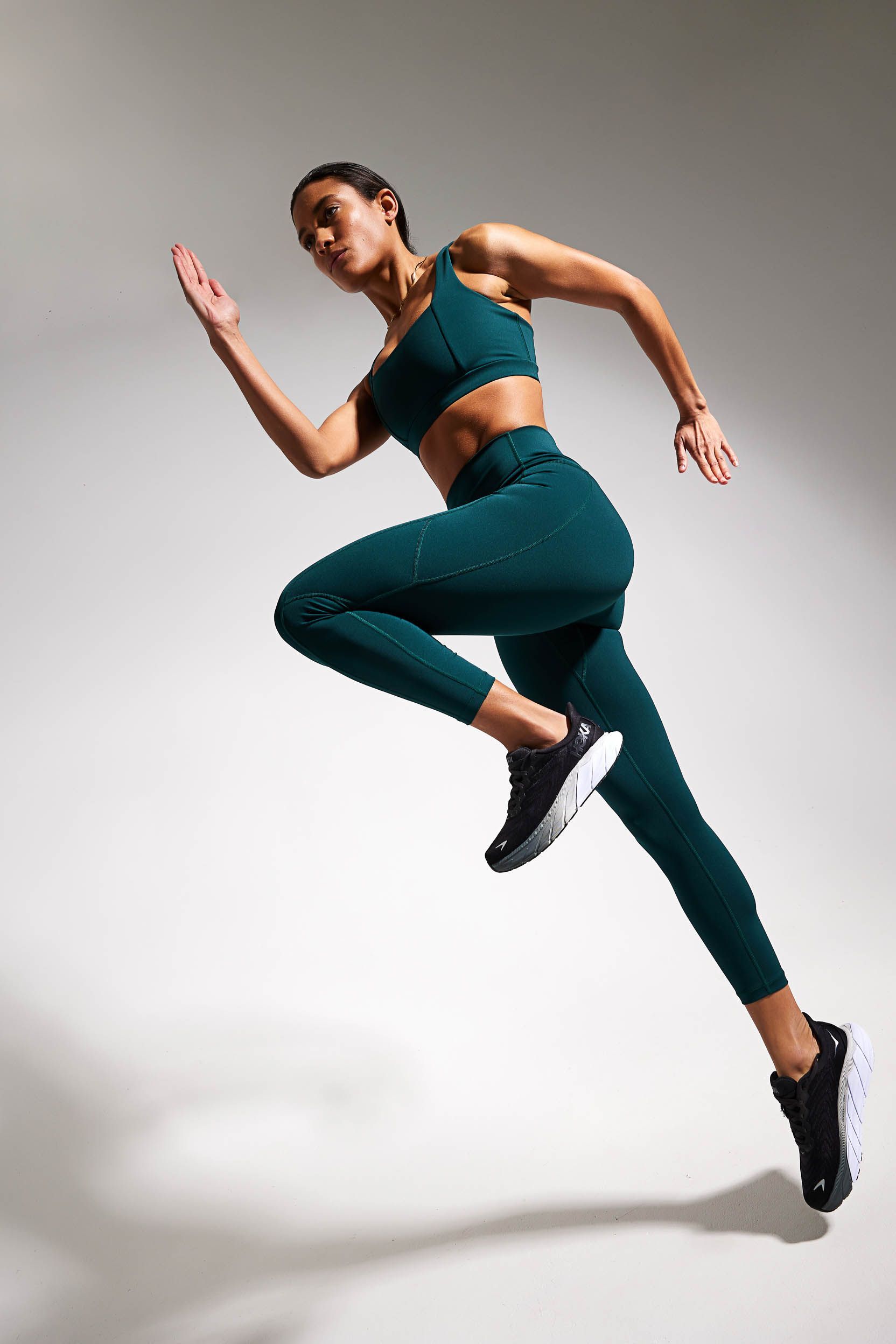 a woman in a green sports bra and leggings is jumping in the air .