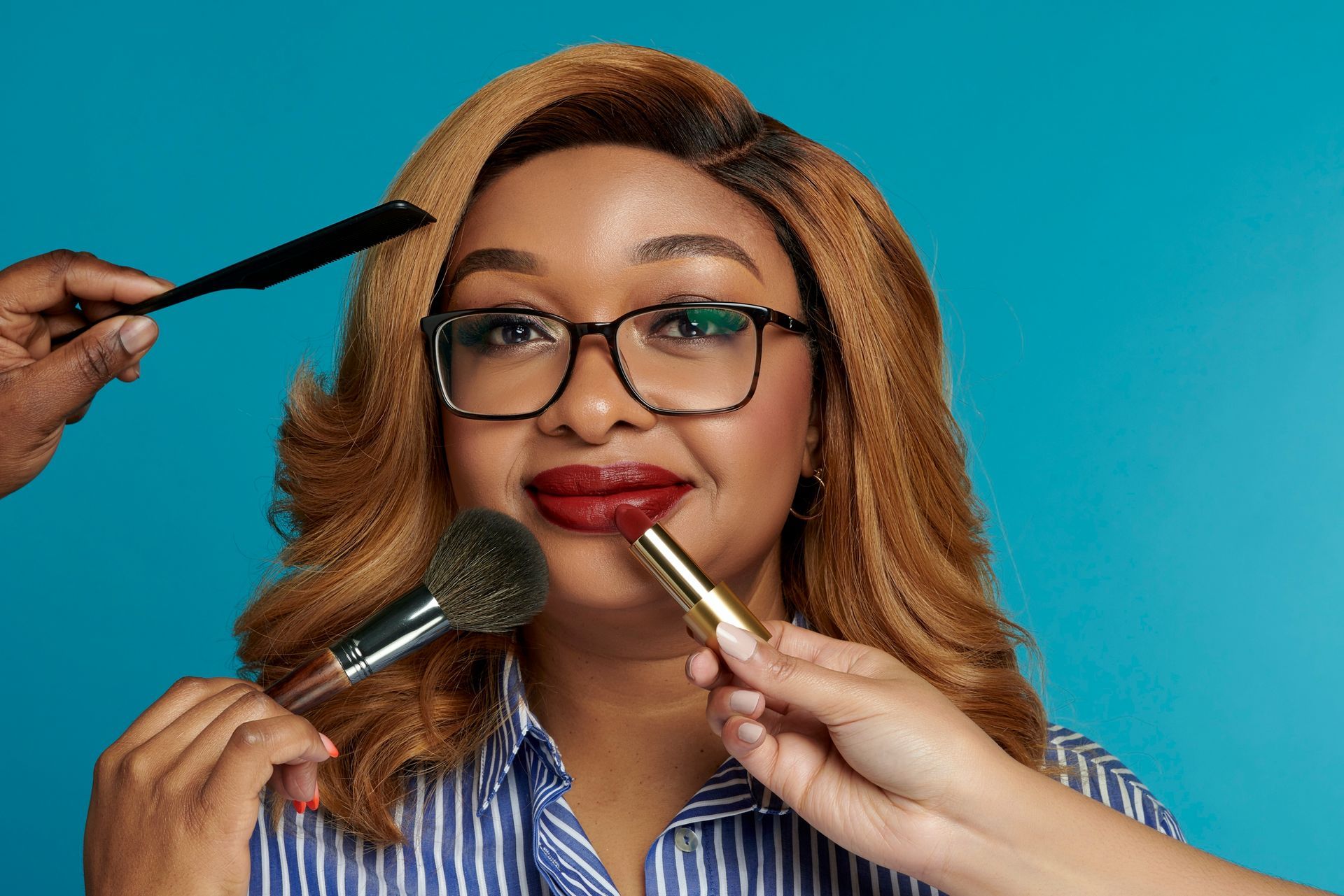 A woman wearing glasses is getting her makeup done by a man.