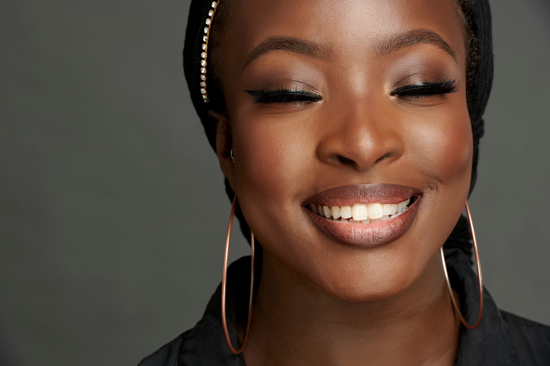 A close up of a woman smiling with her eyes closed and wearing hoop earrings.