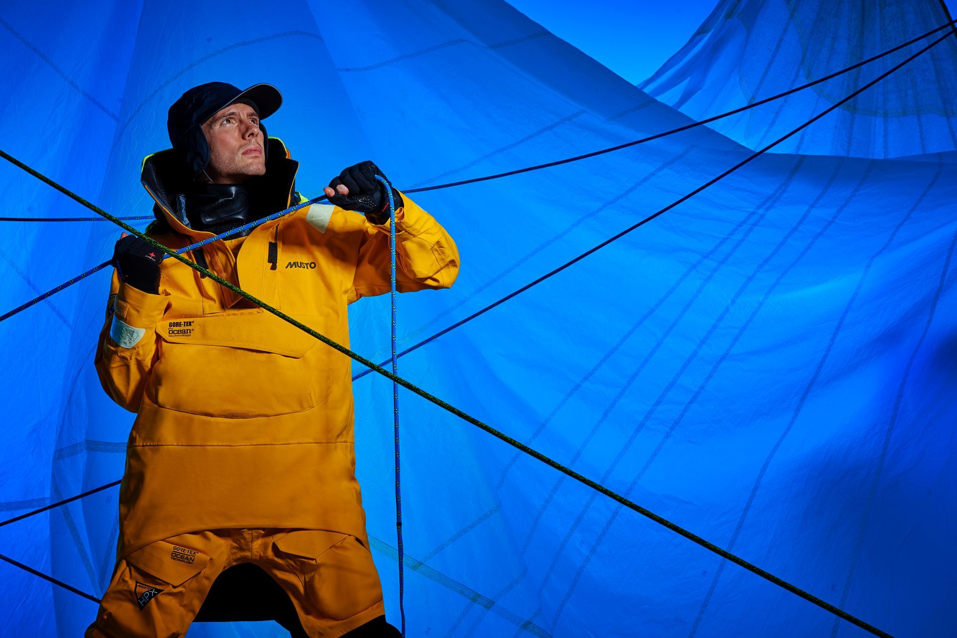 a man in a yellow suit is standing in front of a blue sail .