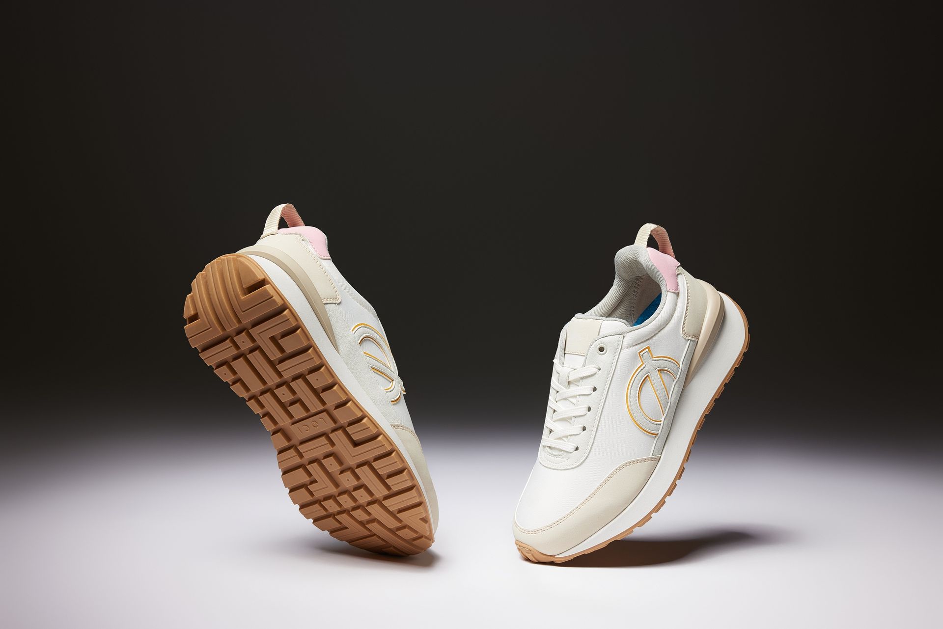 a pair of white sneakers with a brown sole are floating in the air .