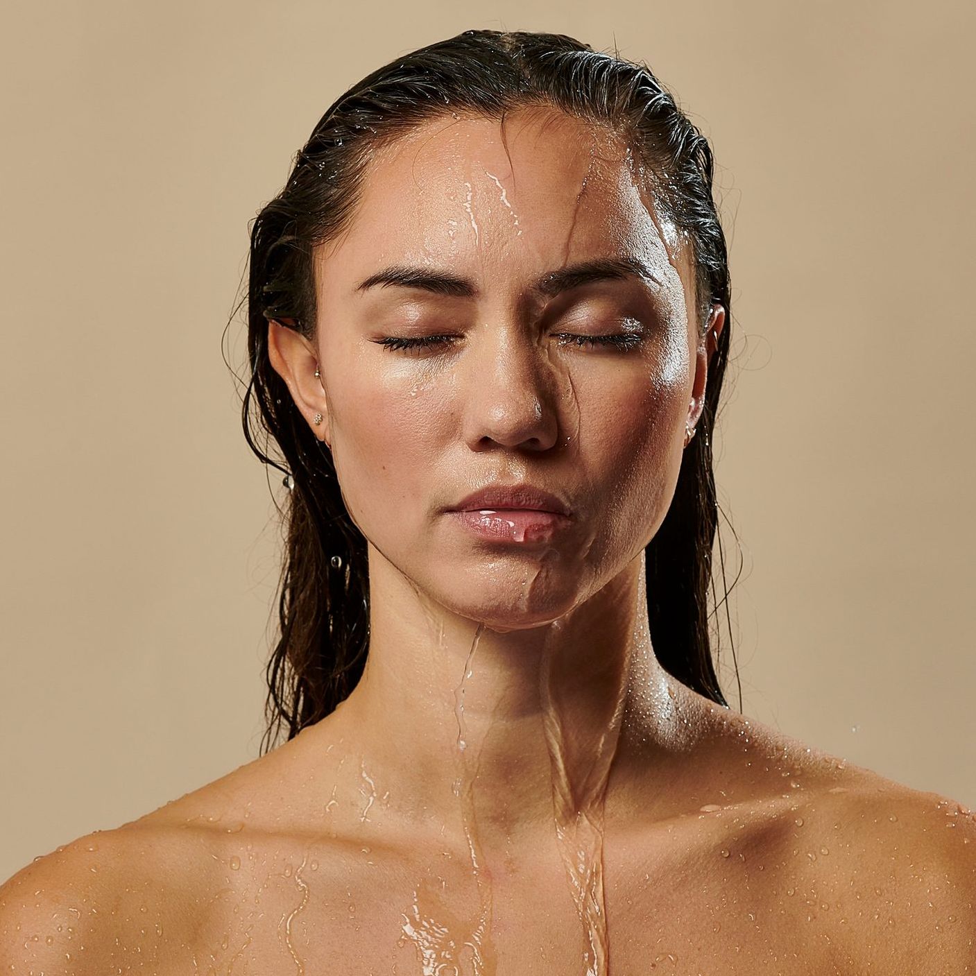 a woman is taking a shower with water pouring on her face .