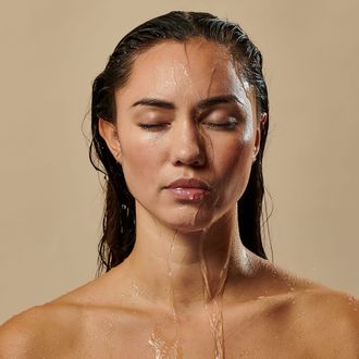 a woman is taking a shower with water pouring on her face .