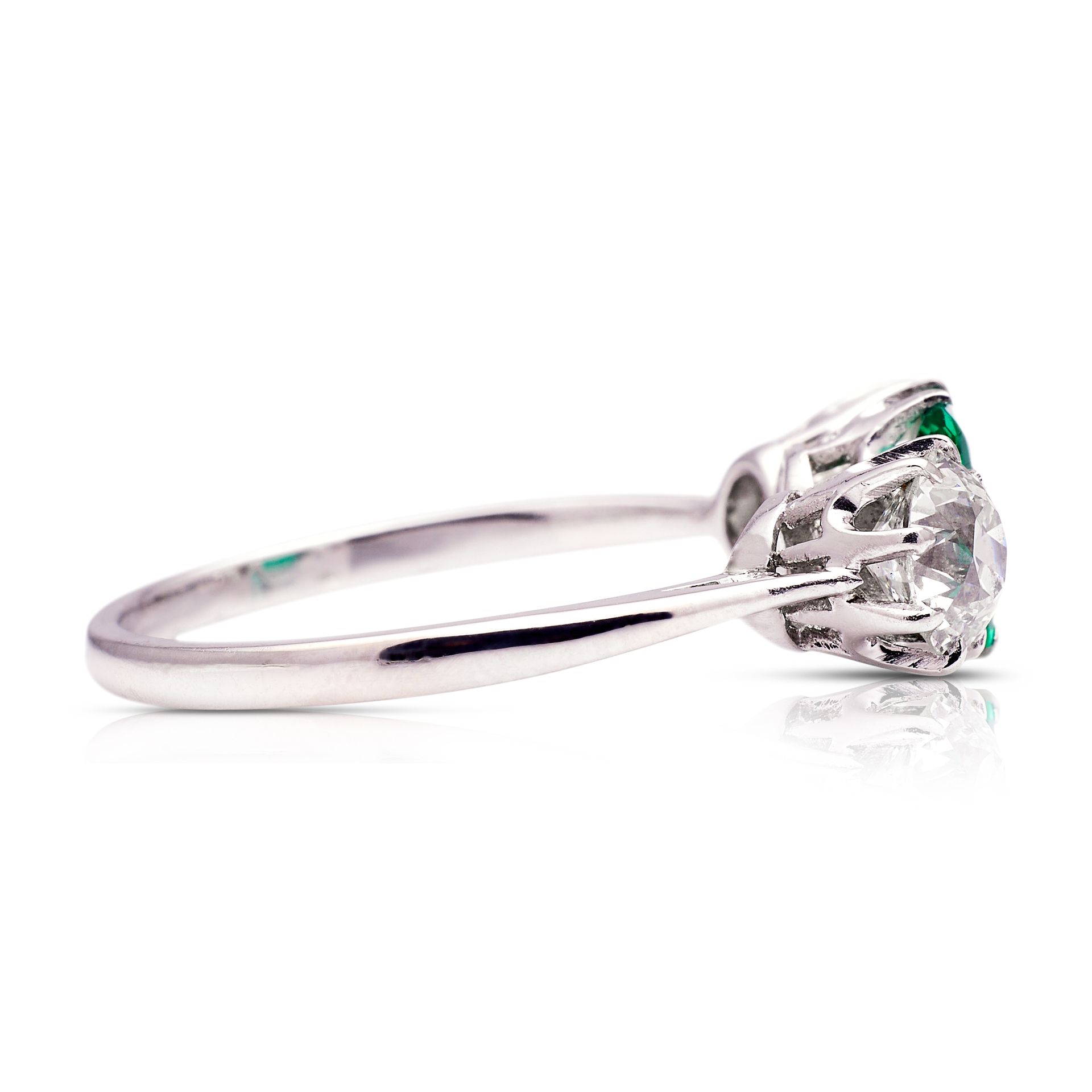 a white gold ring with a diamond and emerald on a white background .