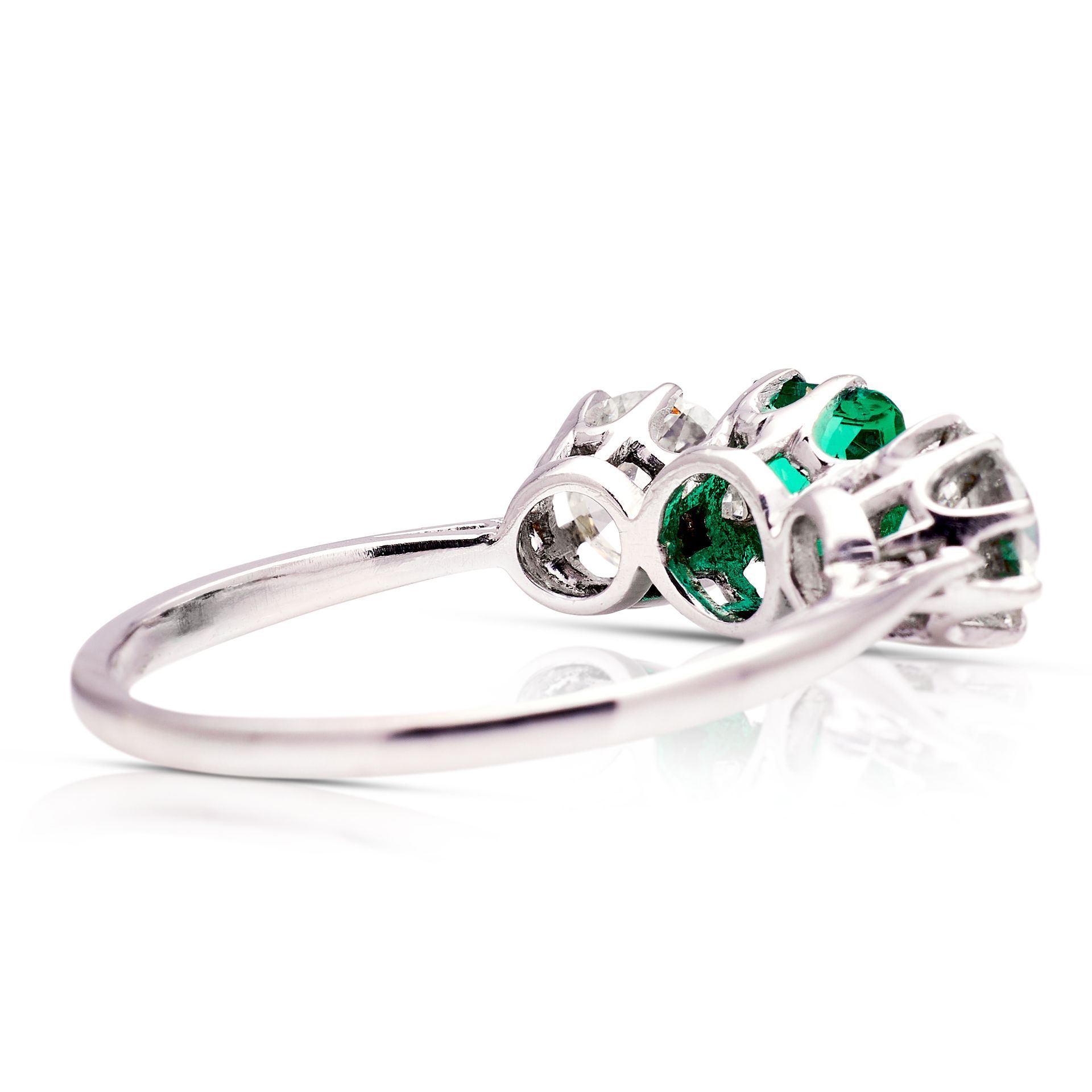 a white gold ring with emeralds and diamonds on a white surface .