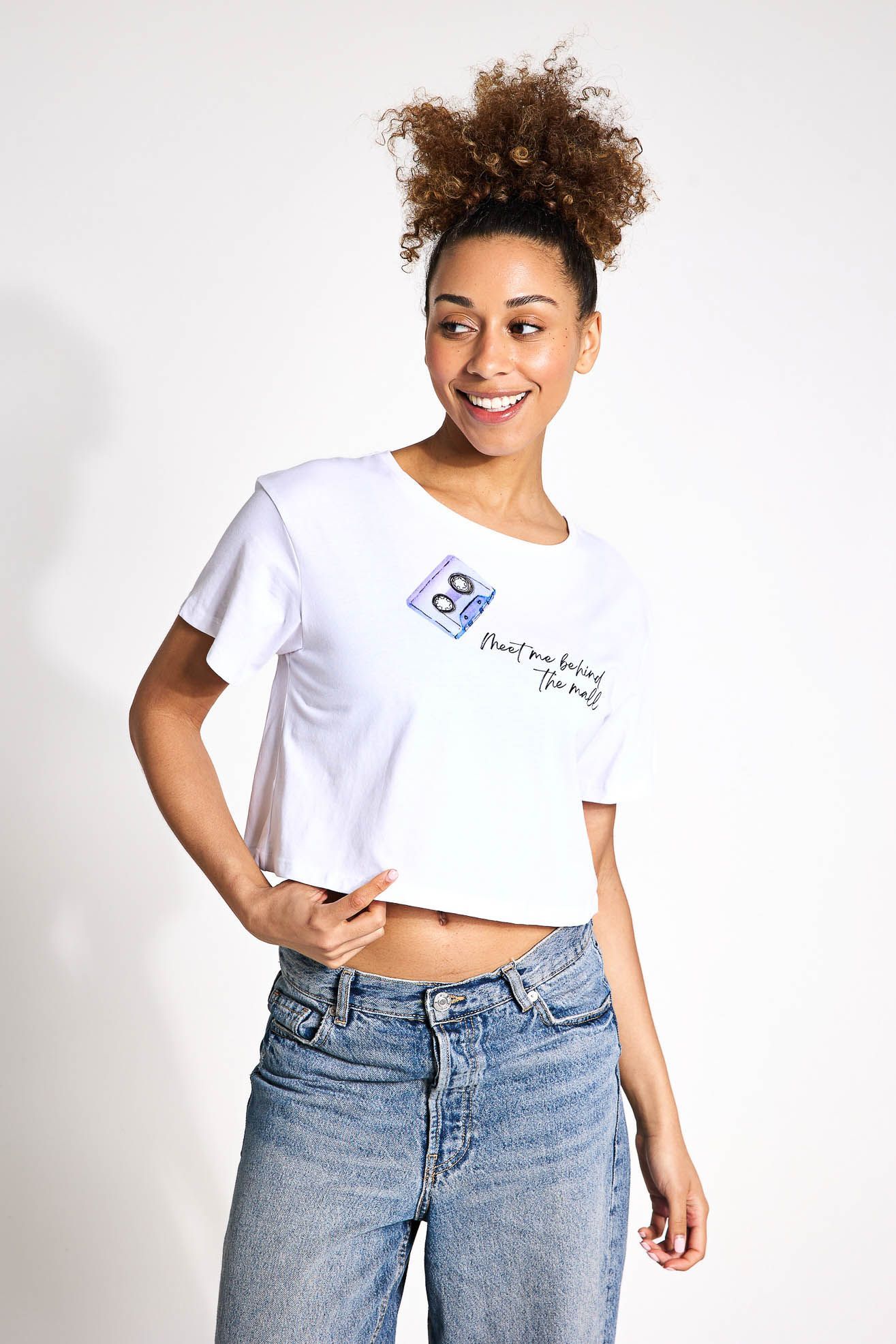 A woman is wearing a white crop top and blue jeans.