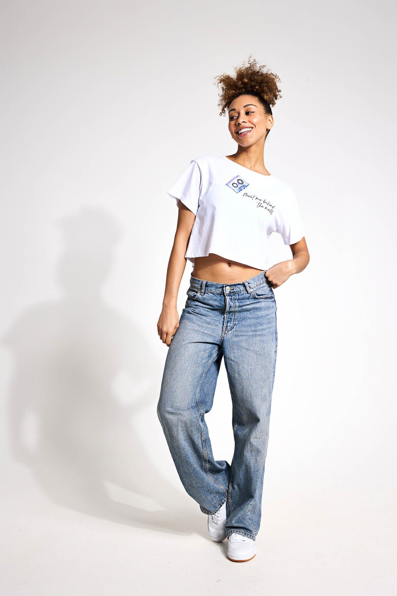 A woman is wearing a white crop top and blue jeans.