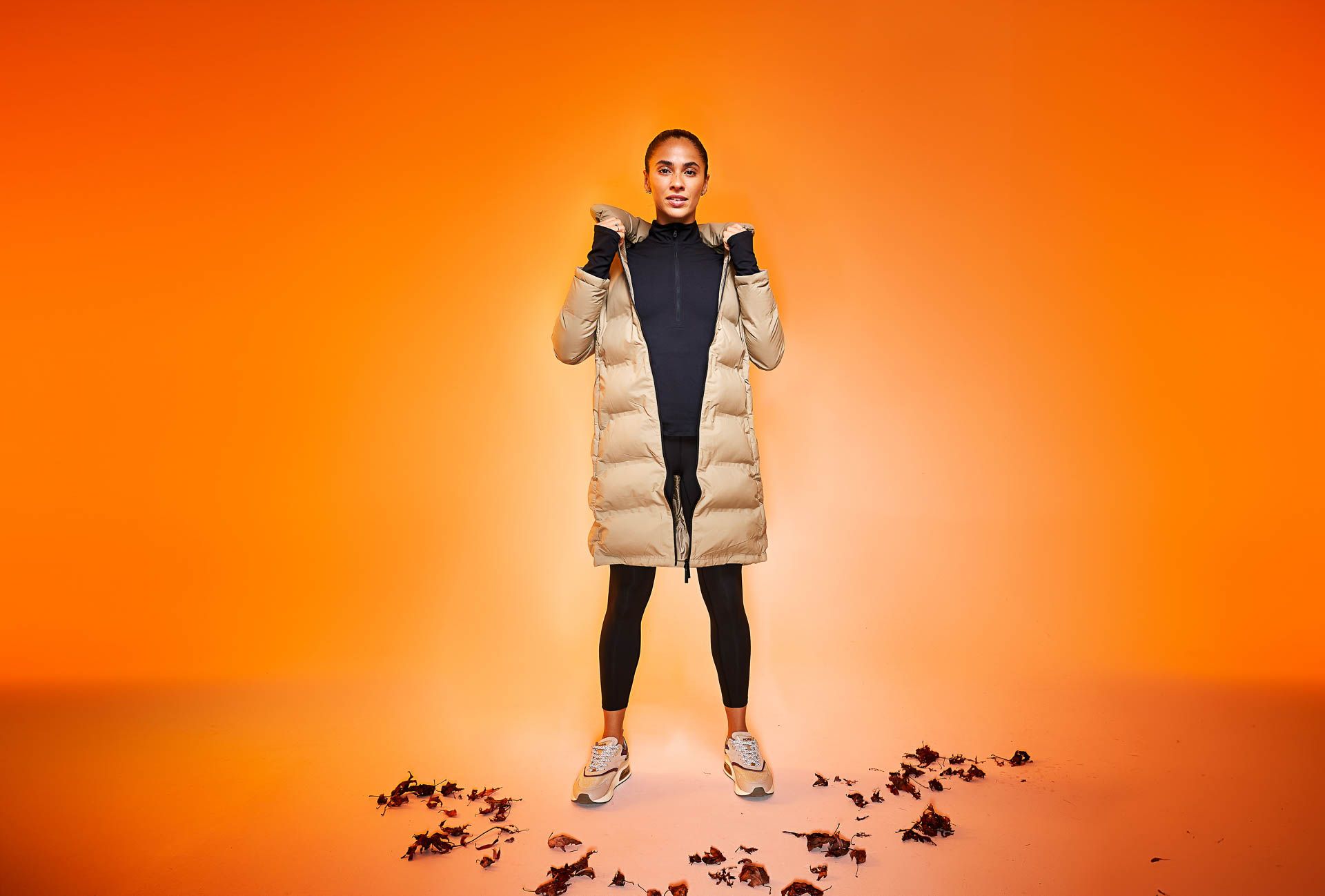 a woman is standing in front of an orange background wearing a padded coat .