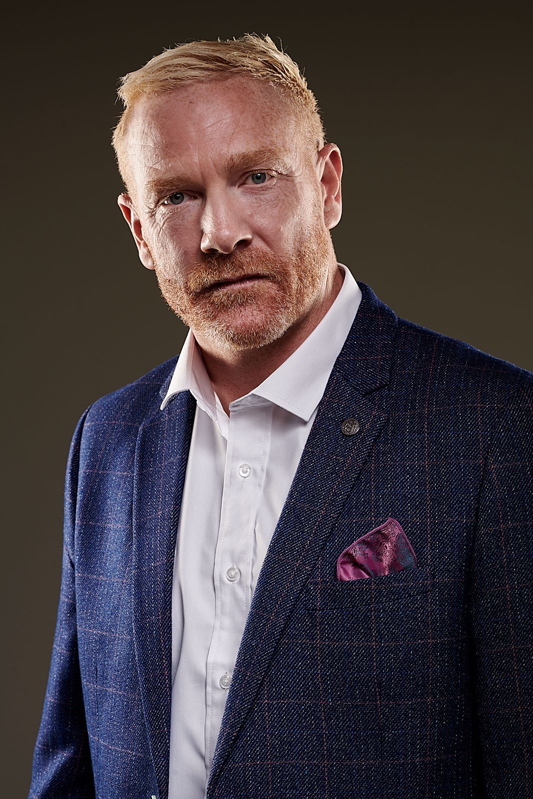 A man with a beard is wearing a blue jacket and a white shirt.