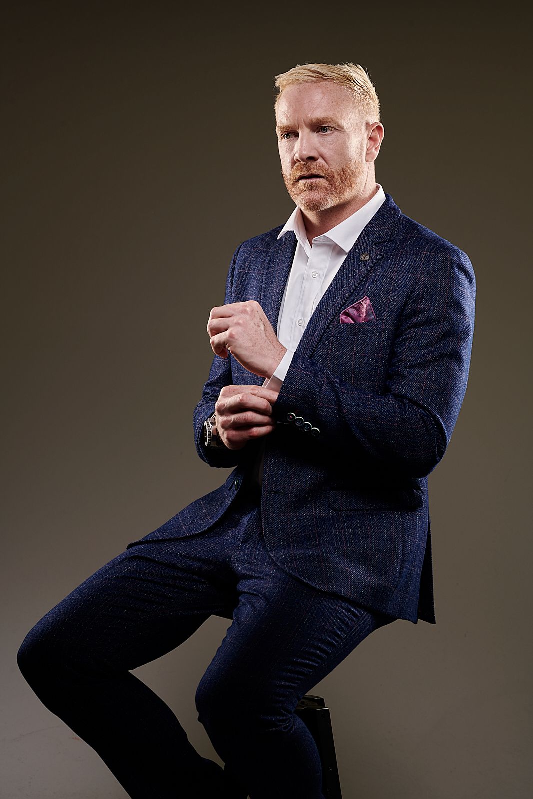 A man in a suit and tie is sitting on a stool.