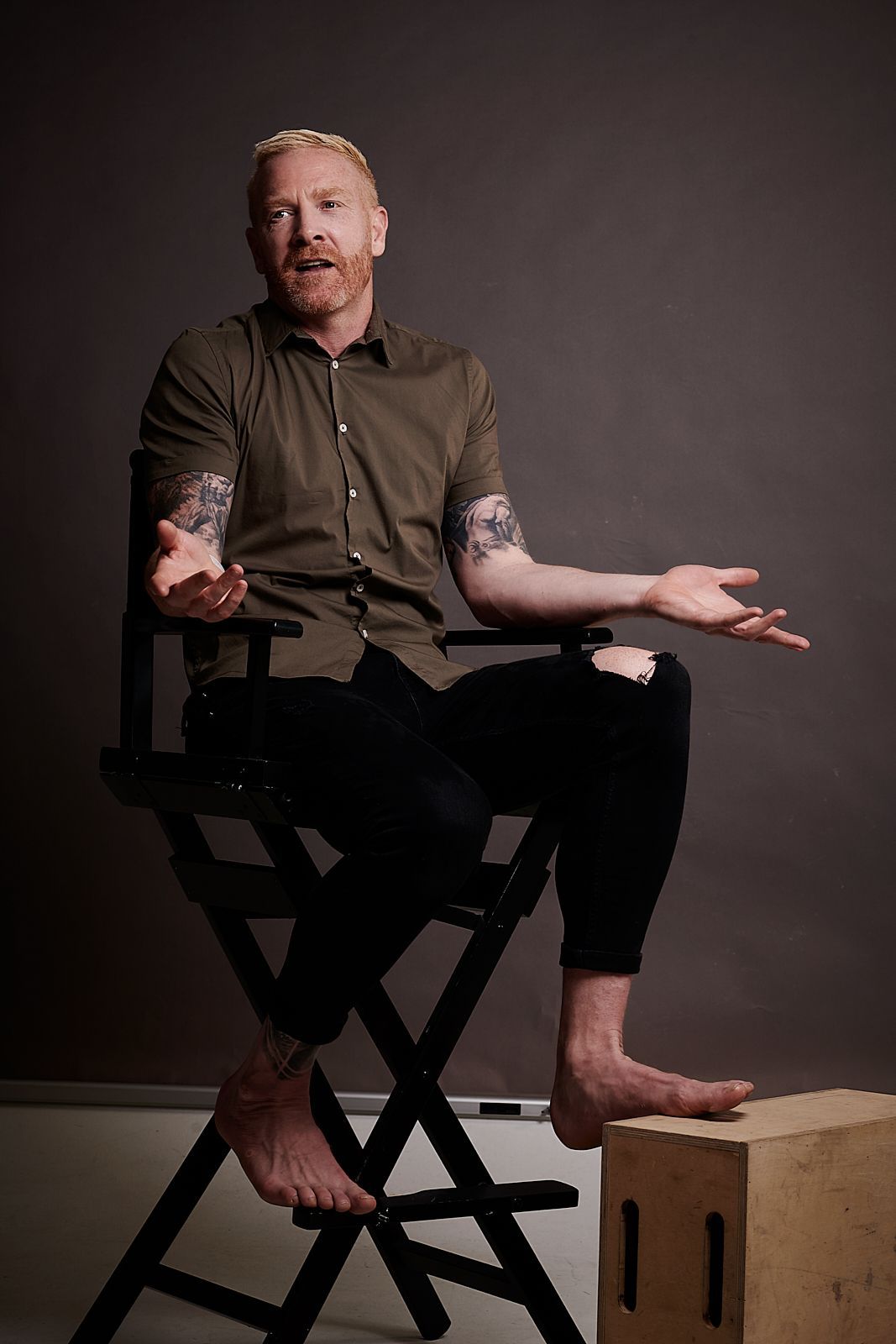 A man is sitting in a director 's chair with his arms outstretched.
