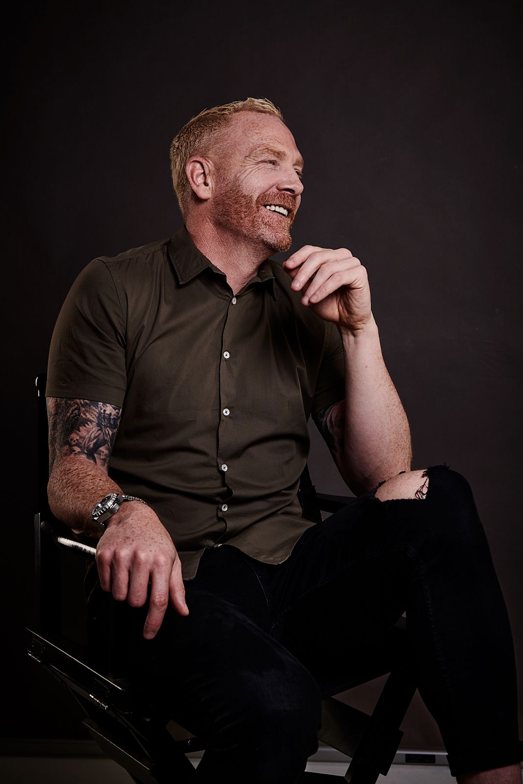 A man with a tattoo on his arm is sitting in a chair and smiling.