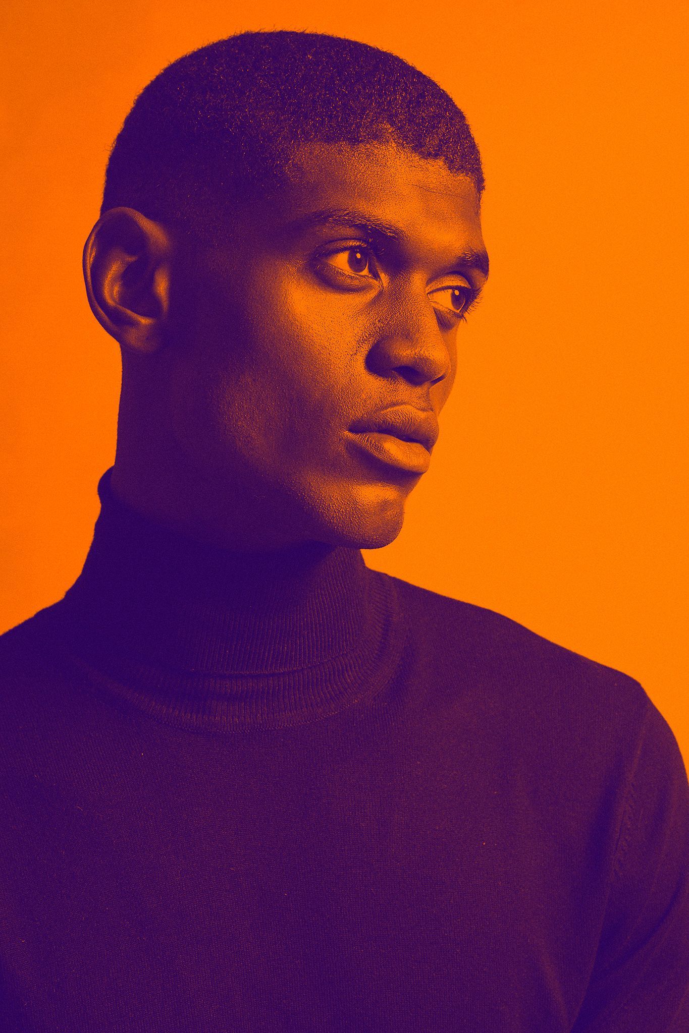 A close up of a man wearing a turtleneck sweater against an orange background.